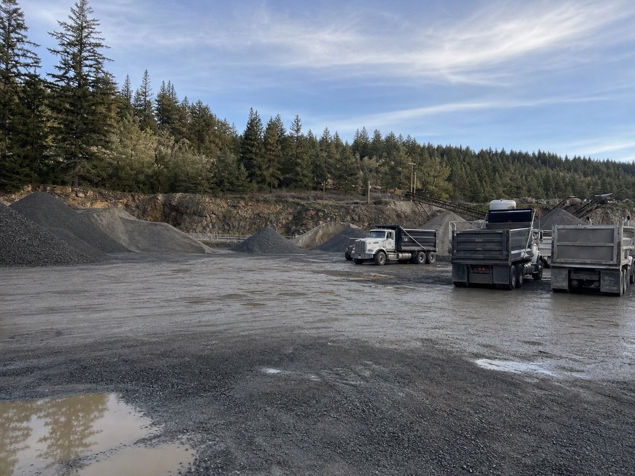 Commercial dump trucks staged beside large aggregate stockpiles