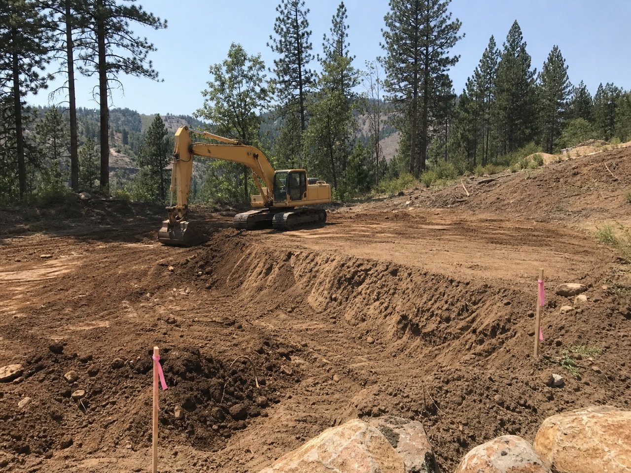 Excavator cutting and leveling a staked building pad